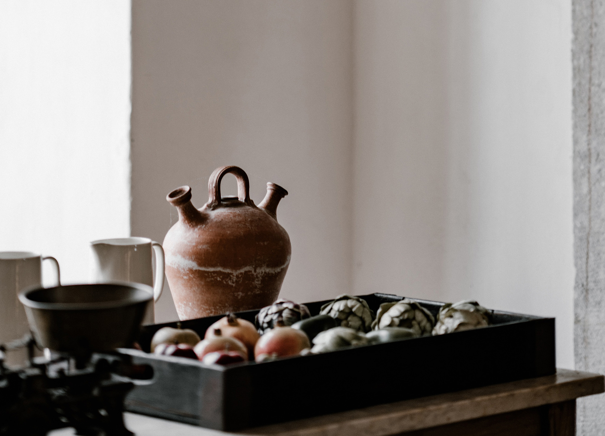 Clay pot and tableware with fruits on wooden table in minimal warm kitchen